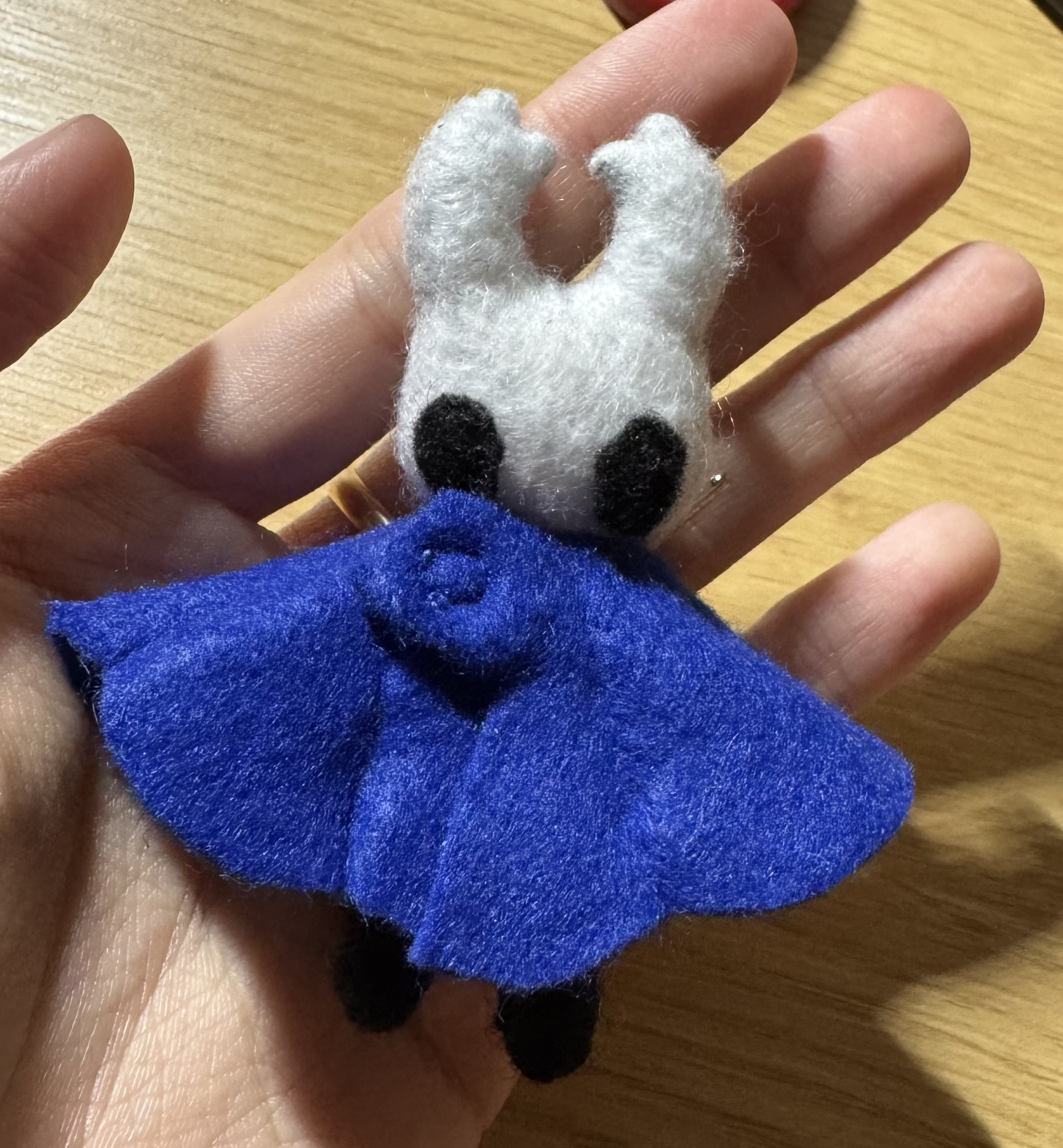The front side of the felt Knight from Hollow Knight held in the artist's left hand