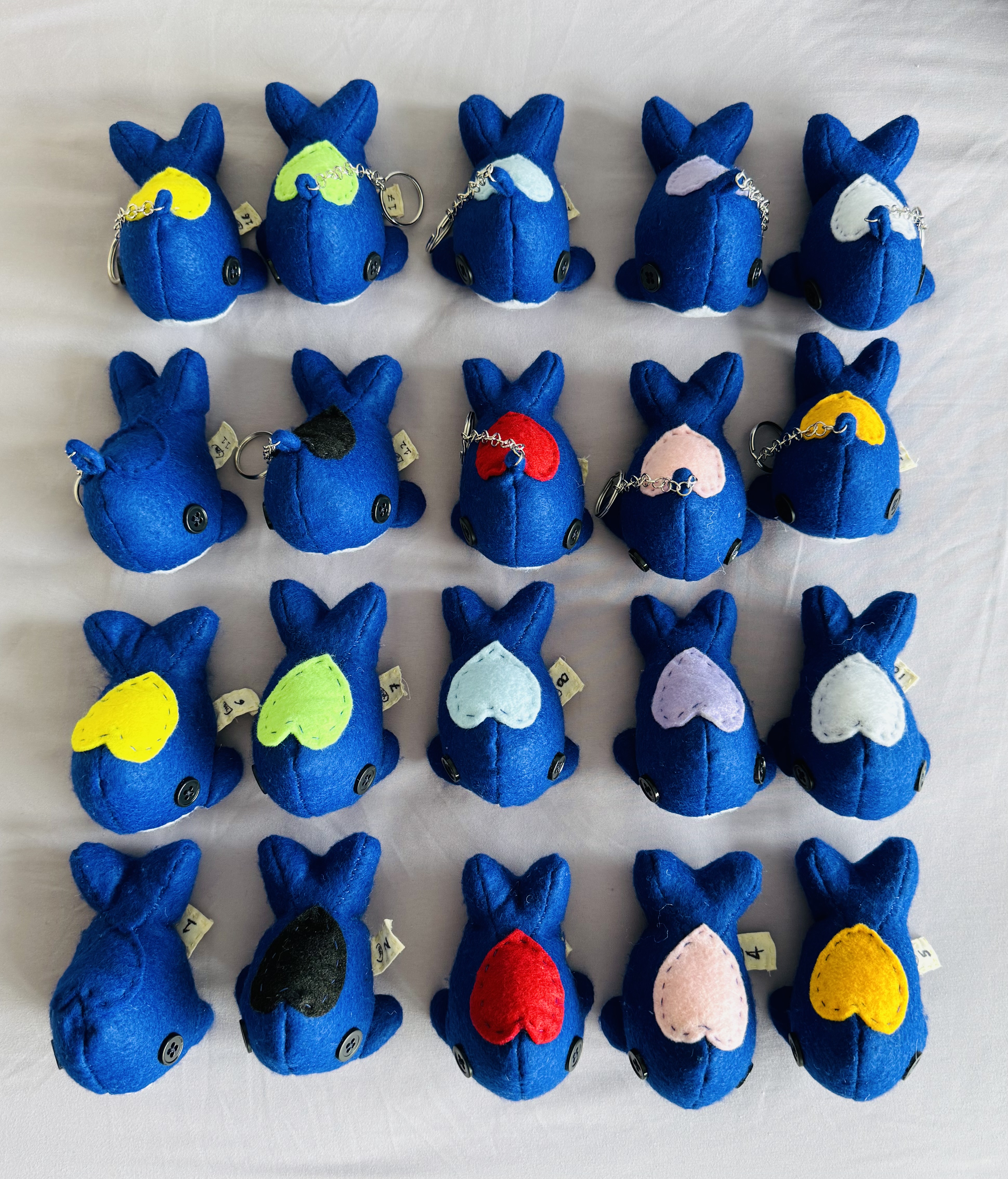 An image of 20 stuffed animal whales arranged in a 5 by 4 grid. The top 10 are keychains while the bottom 10 are just stuffed animals.